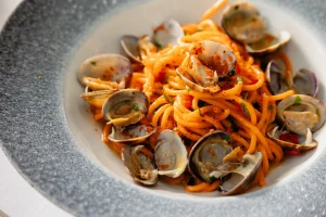 Linguine with clams in a red-tleck tomato sauce, sprinkled with herbs, served in a gray ceramic bowl