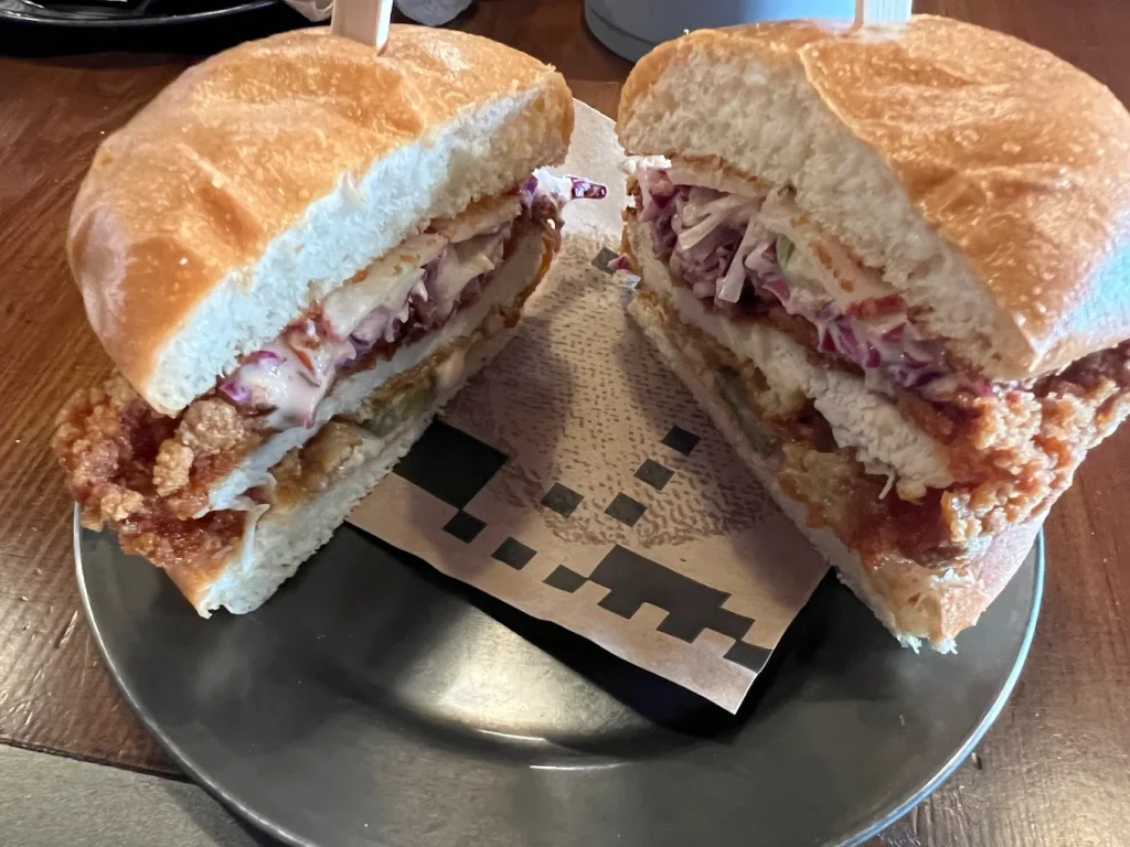 Half sandwich with fried chicken, coleslaw, and sauce on a soft bun, cut in two and served on a plate.