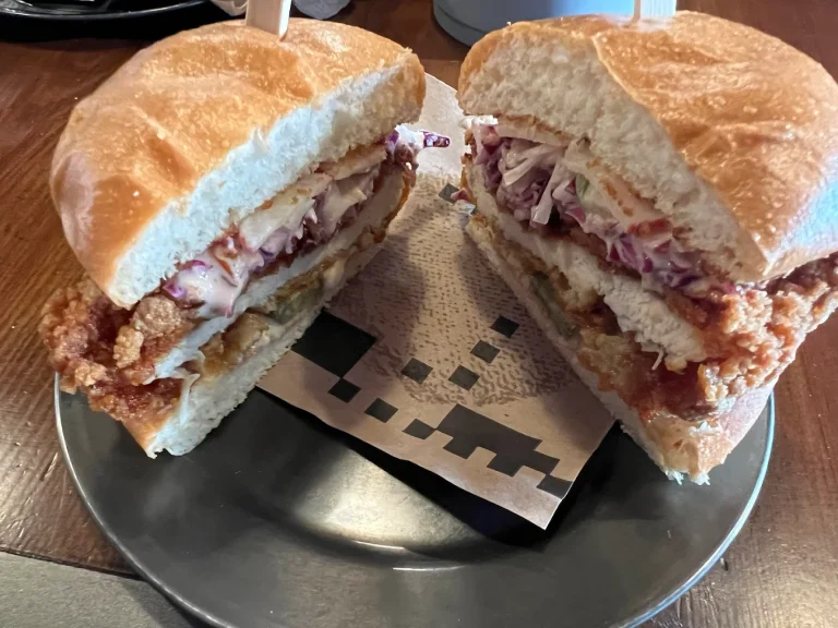 Half sandwich with fried chicken, coleslaw, and sauce on a soft bun, cut in two and served on a plate.