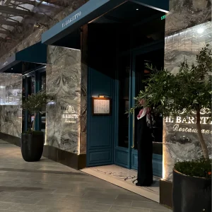 Il Baretto - تَذَوَّقَ Entrance to IL BARETTO restaurant with teal doors, marble walls, and large potted trees outside.