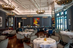 Il Baretto - تَذَوَّقَ Elegant dining room with round tables set for service, white tablecloths, upholstered chairs, and gold spherical chandeliers.