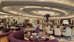Elegant dining hall with circular ornate ceiling, chandeliers, and tables set for service in a luxurious restaurant interior.
