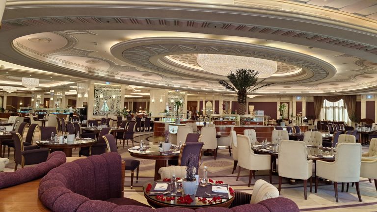 Elegant dining hall with circular ornate ceiling, chandeliers, and tables set for service in a luxurious restaurant interior.